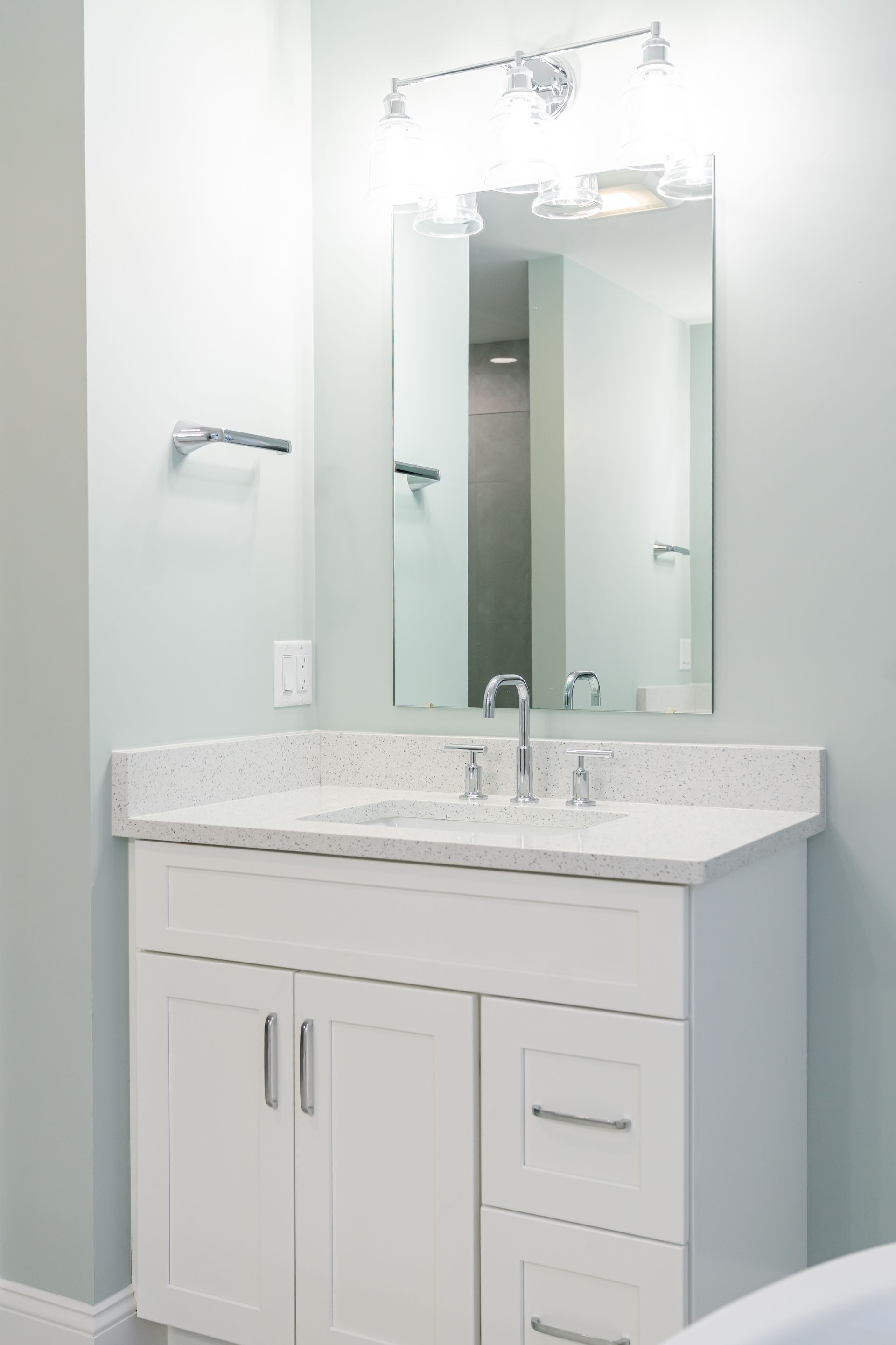 White bathroom vanity with speckled countertop and mirror against a light blue wall