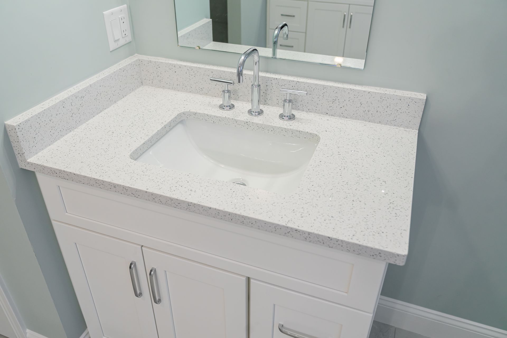 White bathroom vanity with speckled countertop, sink, and chrome faucet against a light blue wall.