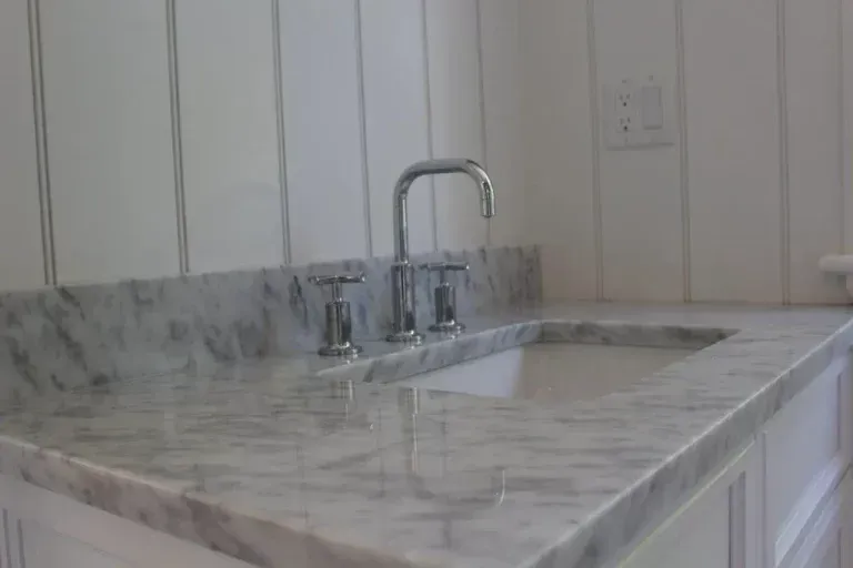 Marble kitchen countertop with built-in sink and chrome faucet against white paneled wall.