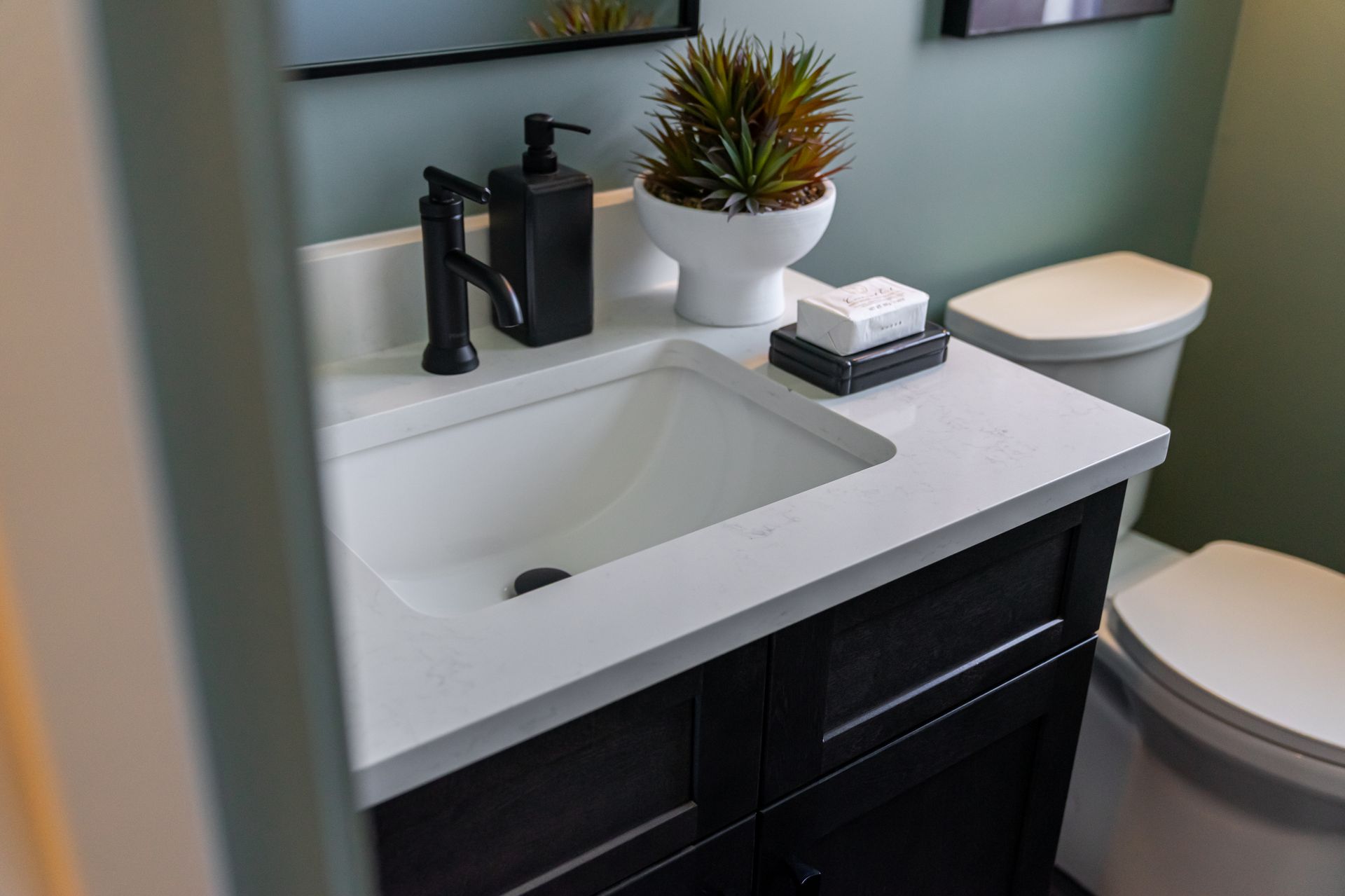 Modern bathroom vanity with white sink, black faucet, dark cabinets, and a toilet beside it