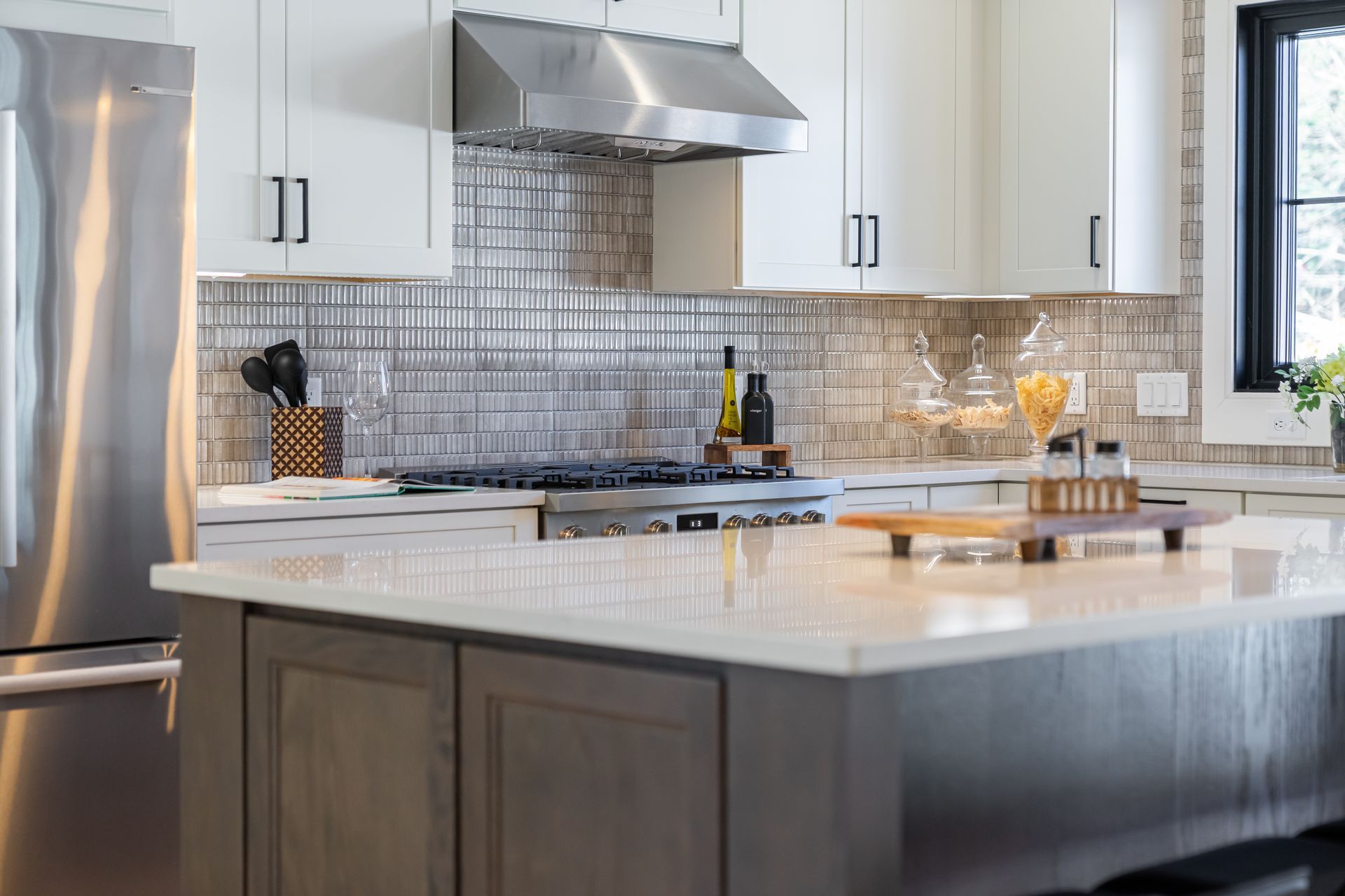 Modern kitchen with white cabinets, stainless steel appliances, a marble island, and a tiled backsplash