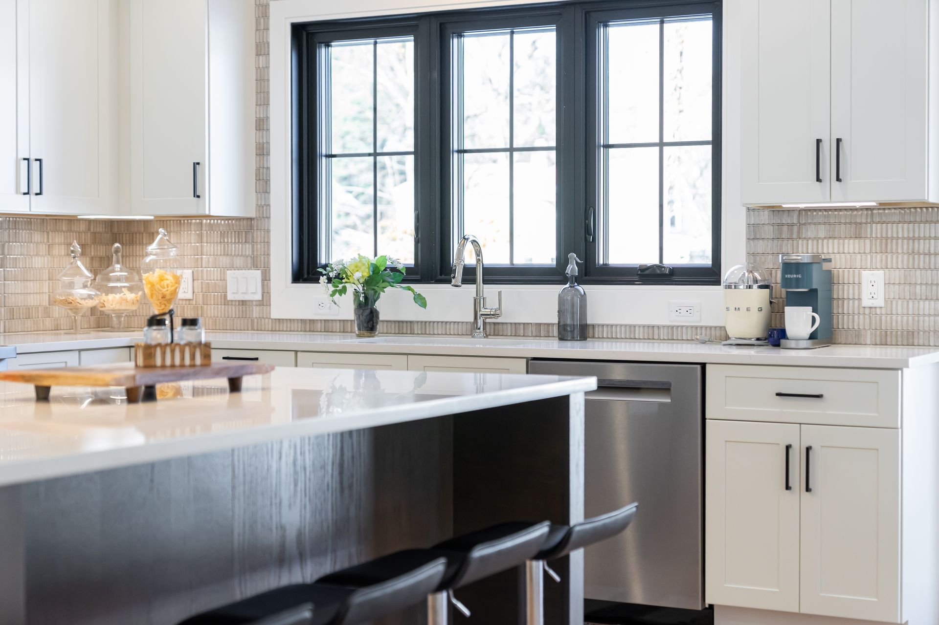 Modern kitchen with white cabinets, black island, and large window above the sink
