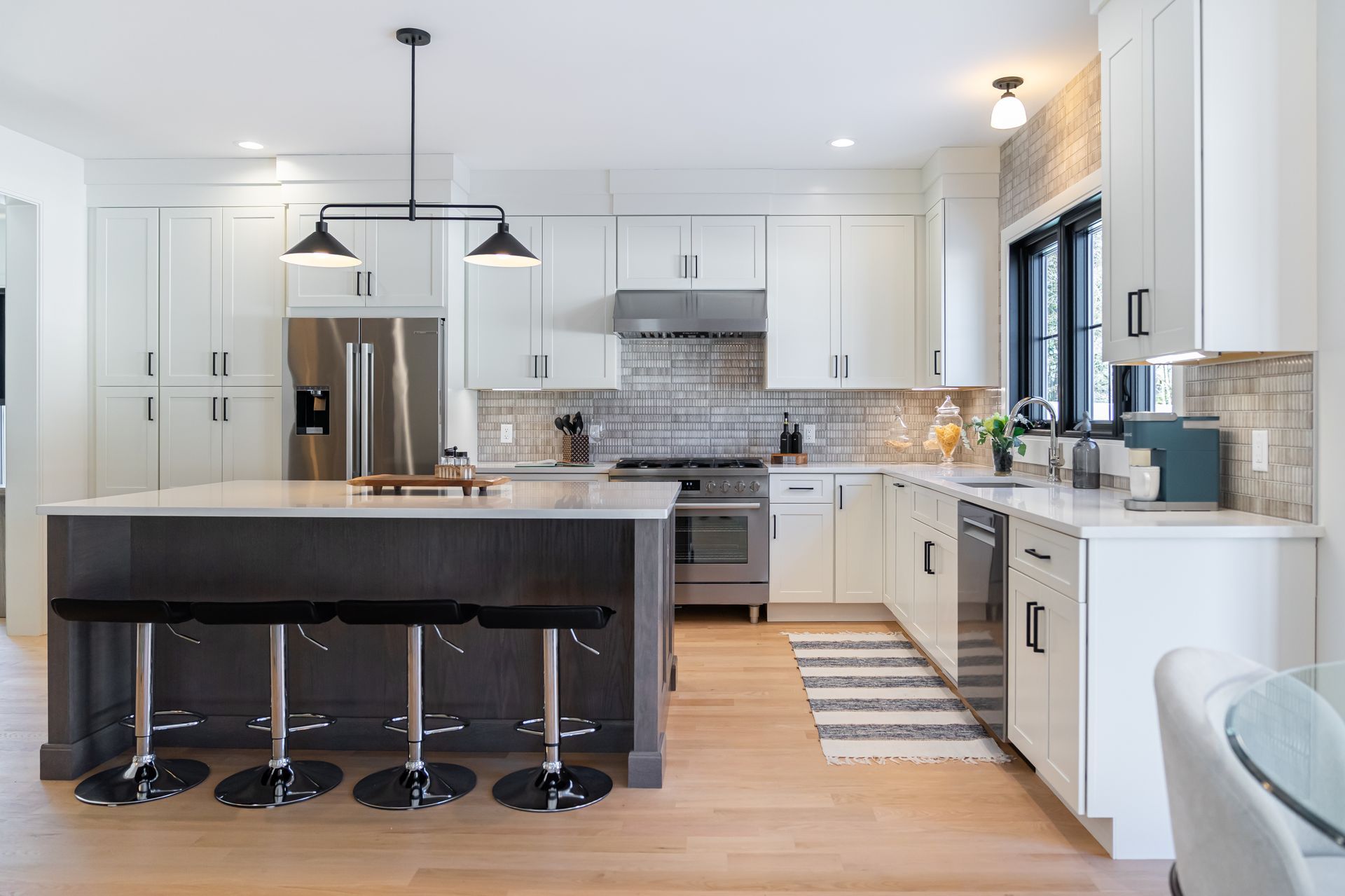Bright modern kitchen with white cabinets, black island stools, stainless appliances, and pendant lights
