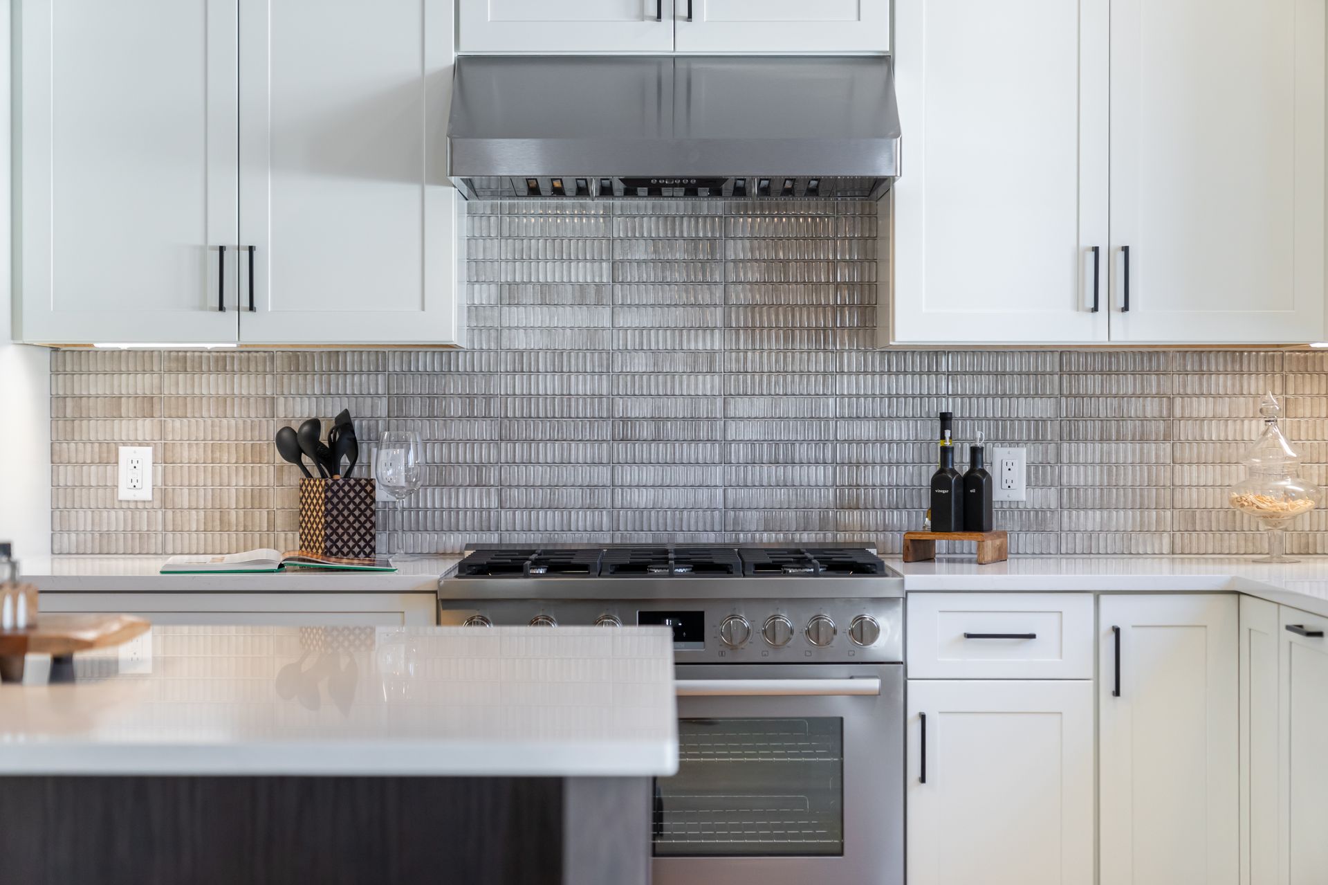 Modern white kitchen with stainless steel stove, tile backsplash, and large island counter