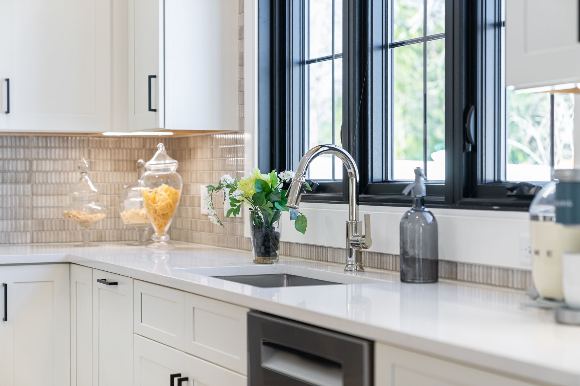 Bright modern kitchen with white cabinets, marble counter, black window, and sink by the window