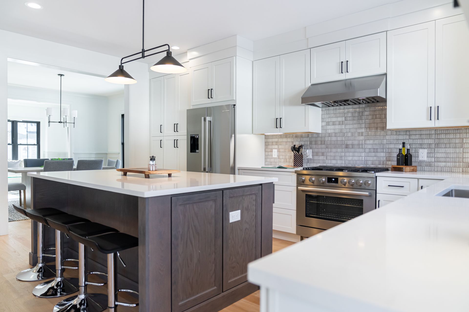 Modern white kitchen with island, pendant lights, stainless range, and dark barstools