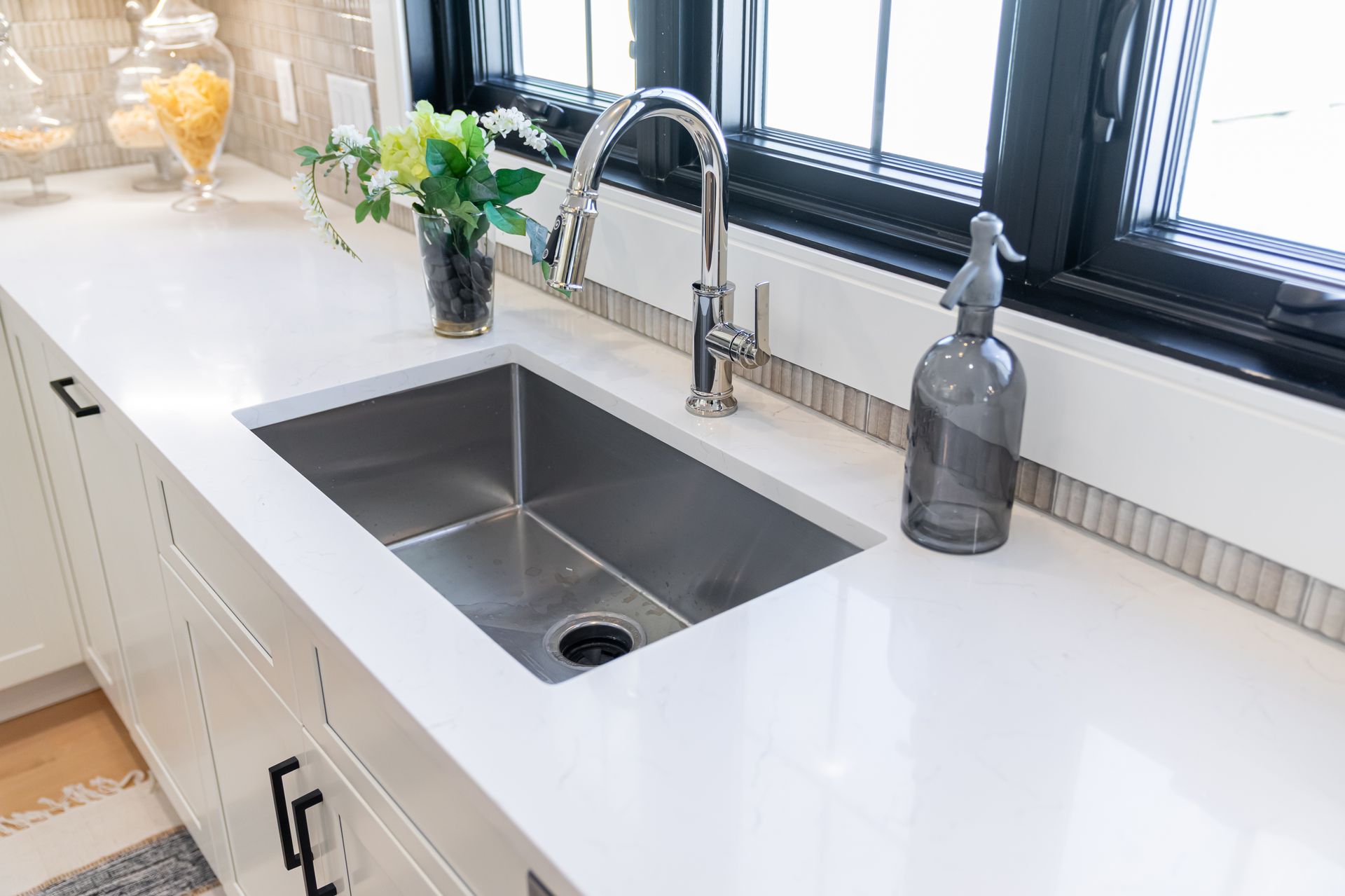 Modern kitchen sink with white countertop, chrome faucet, soap dispenser, and small vase of flowers