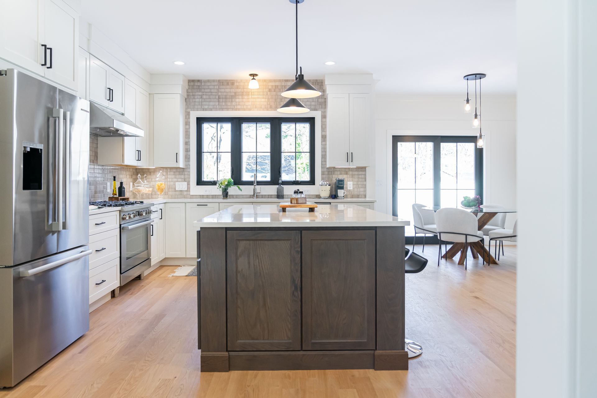 Bright modern kitchen with stainless steel appliances, dark island, and open dining area by windows