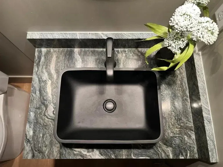 Black square sink with chrome faucet on gray marble vanity, with white flowers on the right