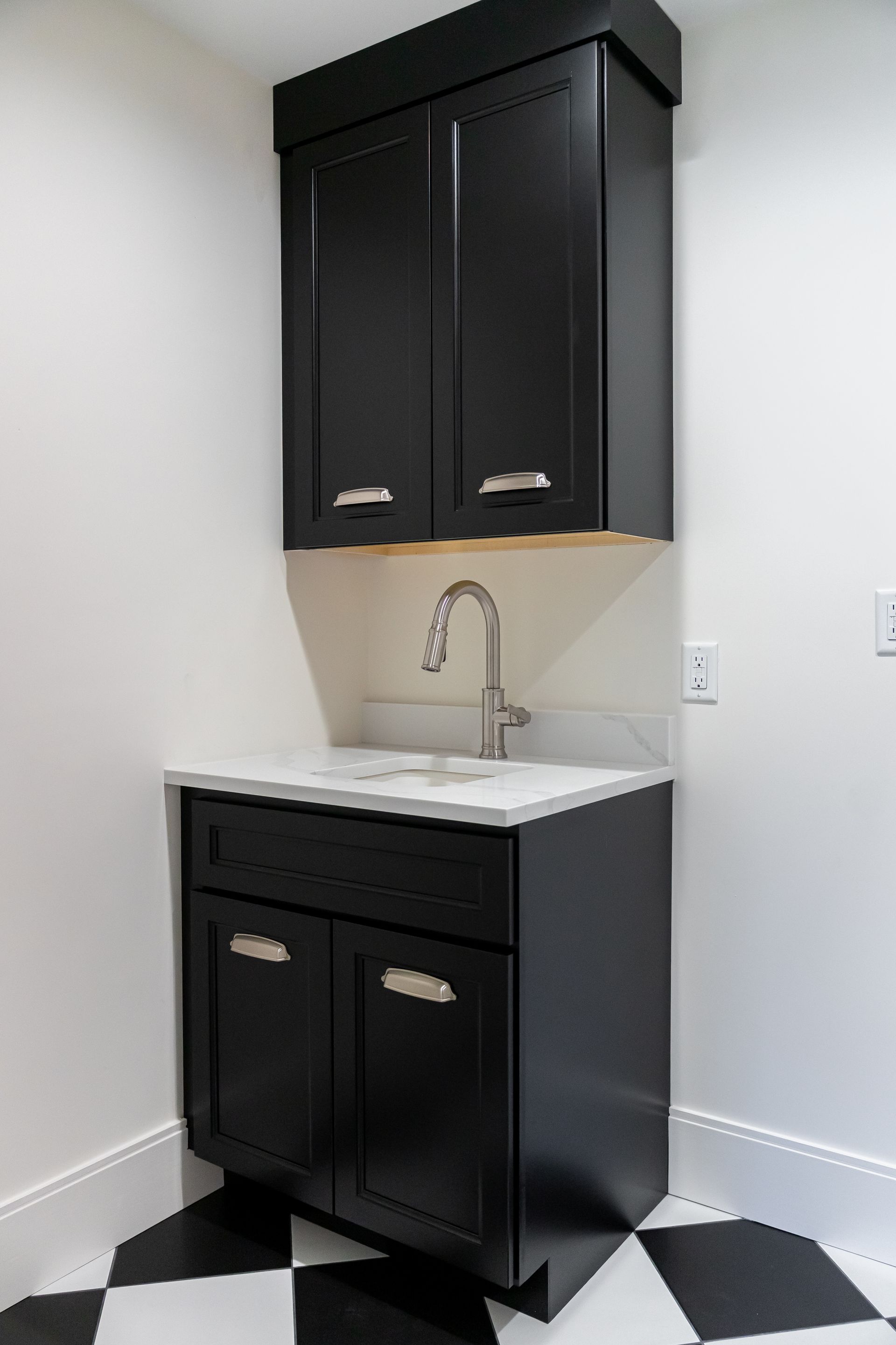 Black bathroom vanity with white sink and mirror-front cabinet against a white wall on a checkered floor