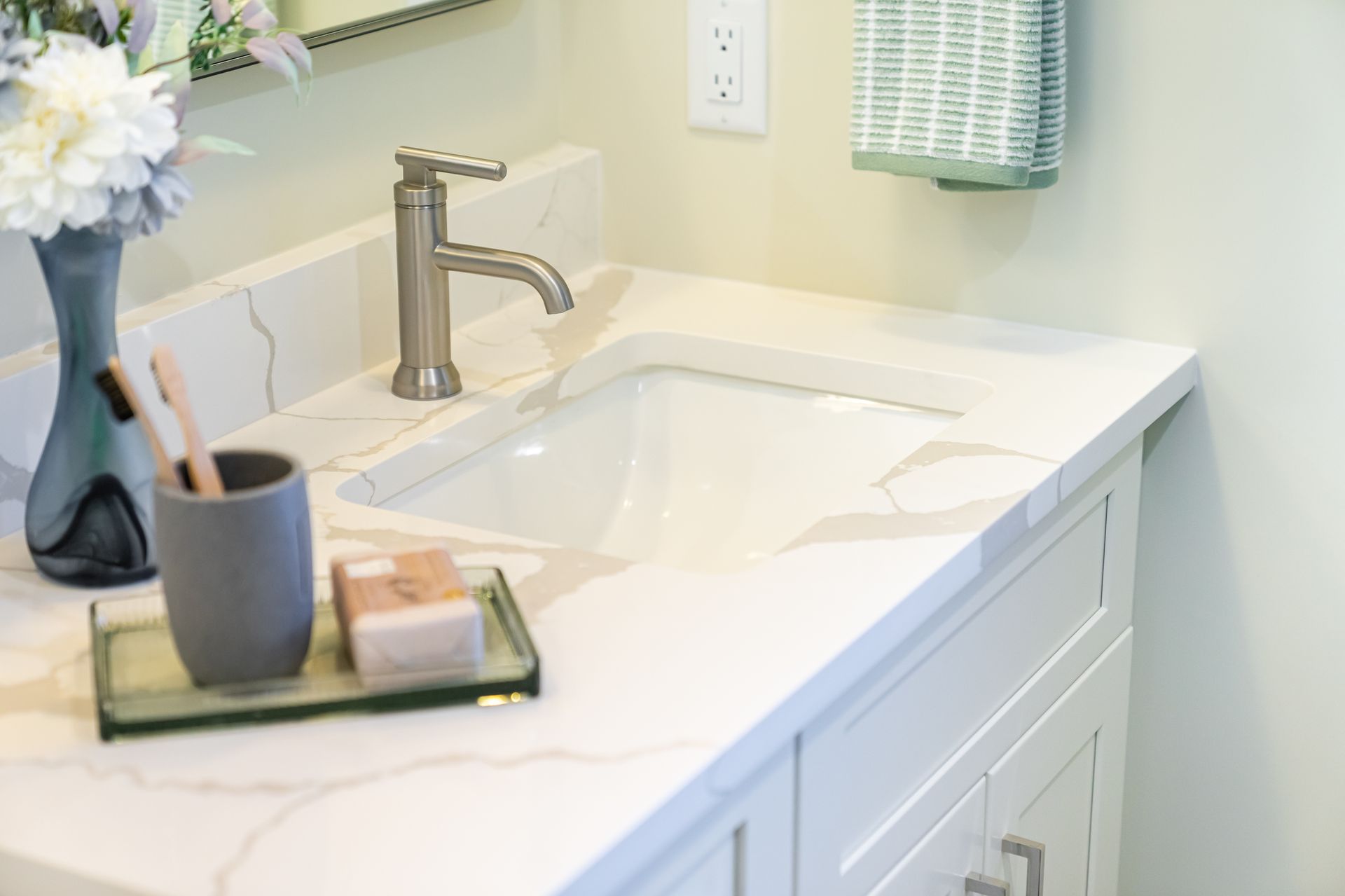 White bathroom vanity with a sink, chrome faucet, and countertop tray with toiletries and flowers