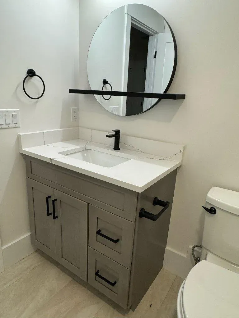 Modern bathroom vanity with round mirror, black faucet, and toilet beside it