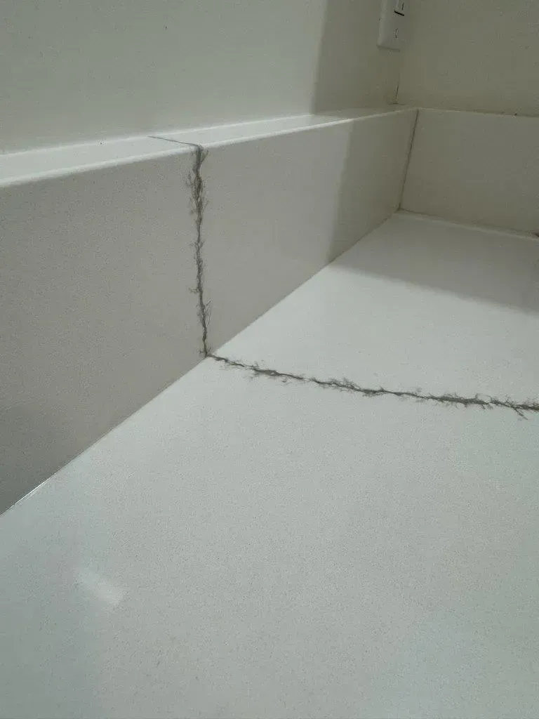 White tiled corner with visible cracks along the wall and floor seam