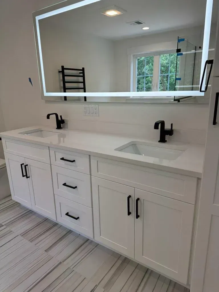 Bright white bathroom vanity with double sinks, black fixtures, and large mirror beneath a window.