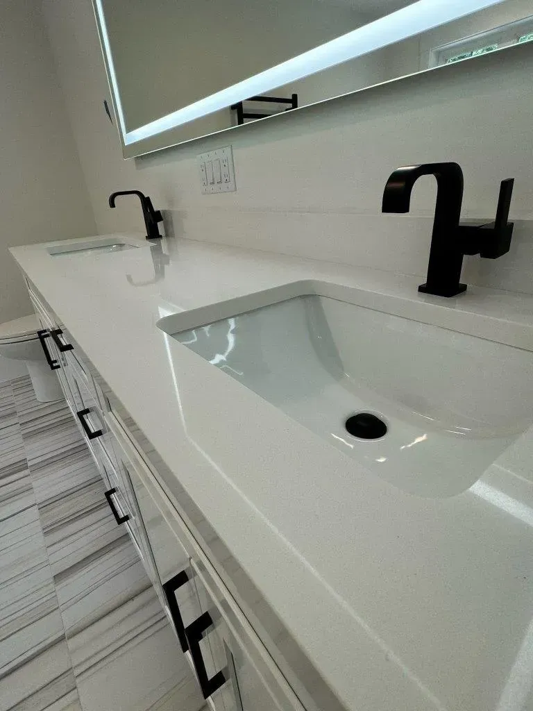 Modern bathroom vanity with two white sinks and matte black faucets beneath a large mirror.