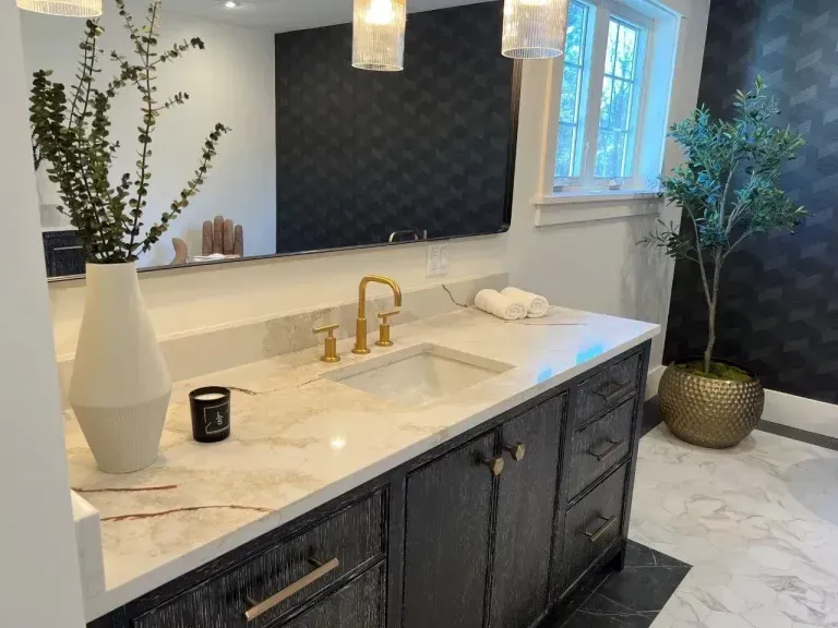 Elegant bathroom vanity with marble countertop, gold faucets, dark cabinets, and white vase decor