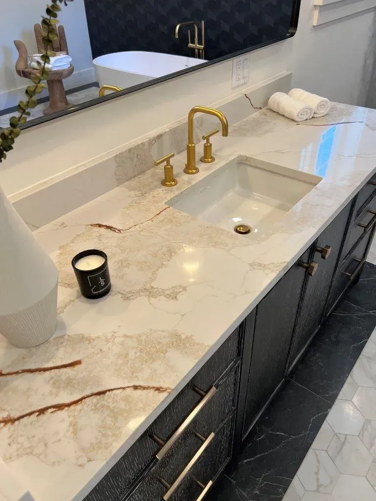 Marble bathroom vanity with gold faucet, undermount sink, candle, and folded towels.