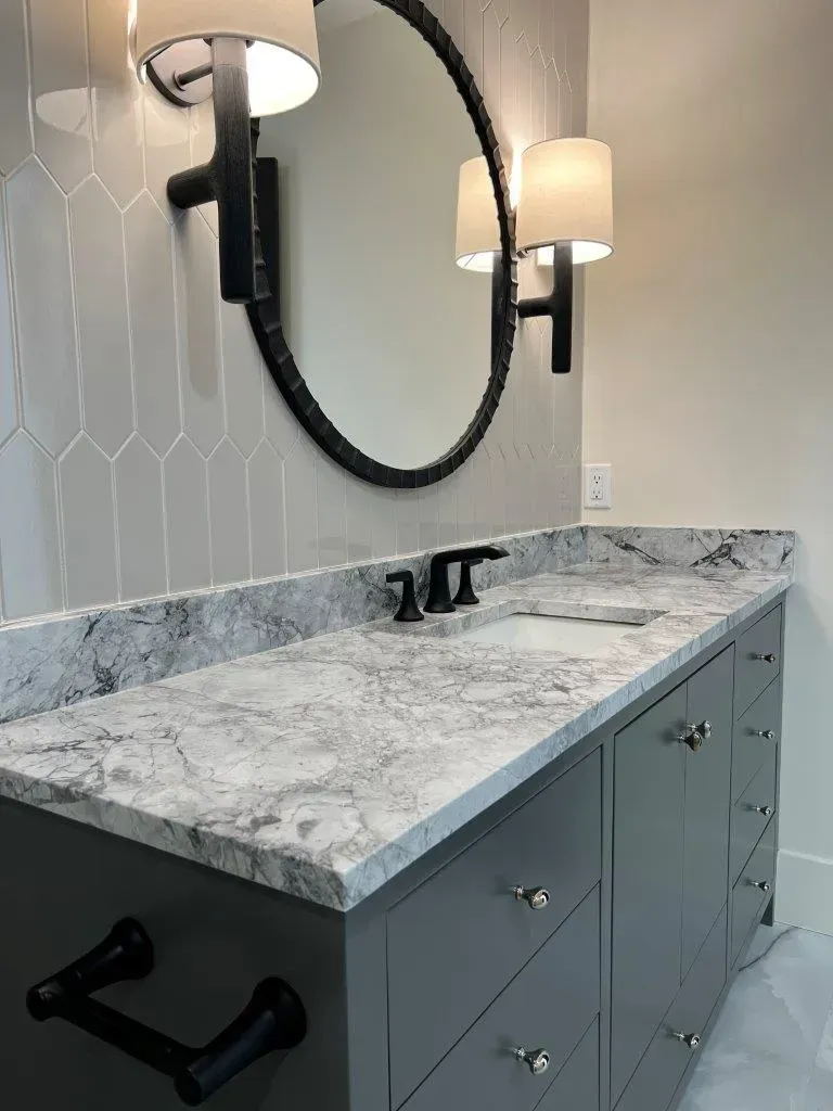 Modern bathroom vanity with gray marble countertop, black faucet, oval mirror, and wall sconces