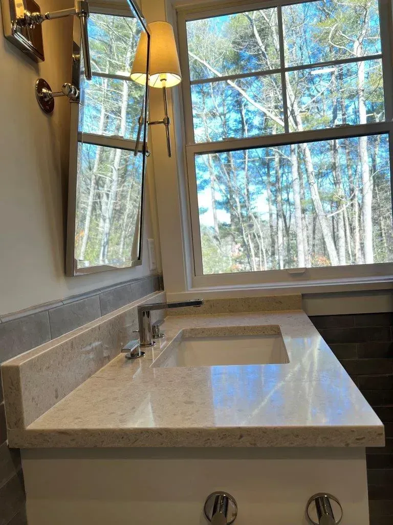 Modern bathroom vanity with sink and mirror beside a large window overlooking trees
