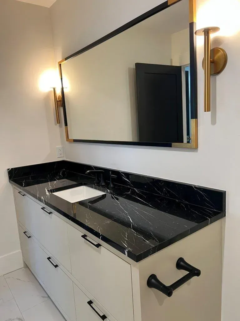 Modern bathroom vanity with black marble countertop, large mirror, and wall sconces.