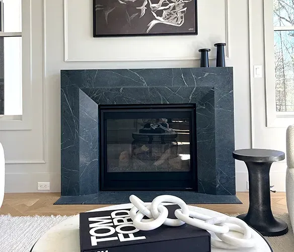 Modern living room with dark stone fireplace, framed art, and black-and-white decor objects