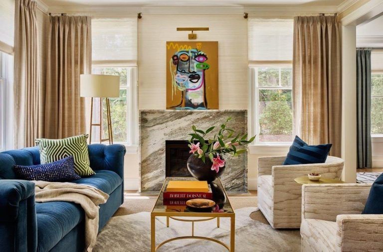 Elegant living room with blue and cream sofas, marble fireplace, and colorful artwork above the mantel