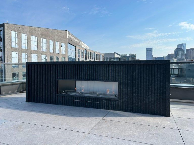 Modern rooftop terrace with a black fireplace structure and city buildings in the background