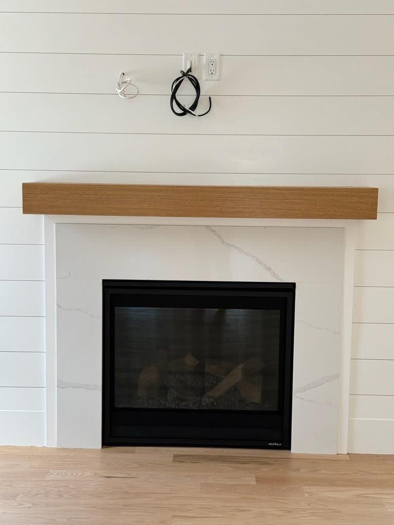 White shiplap fireplace with wood mantel and black glass insert in a bright room