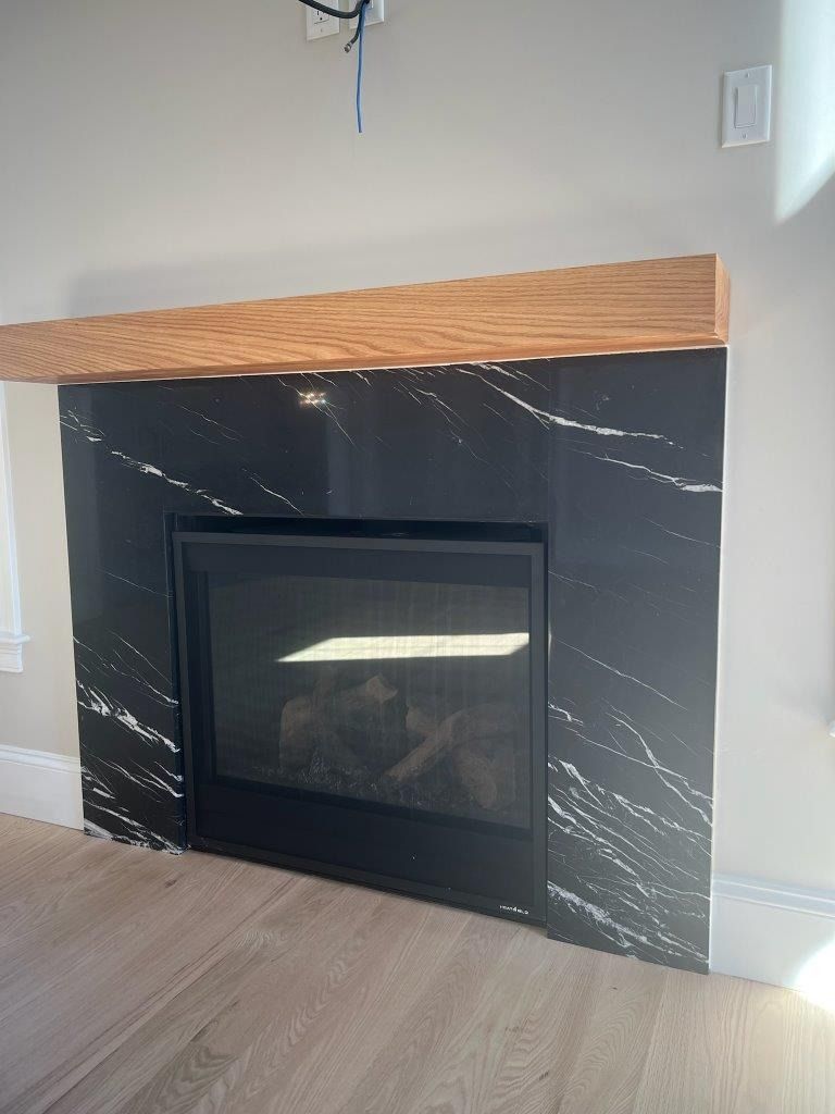 Modern fireplace with black marble surround, wood mantel, and glass insert in a light-colored room