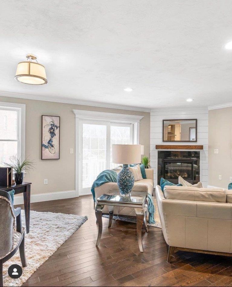 Bright living room with beige sofas, blue lamp, fireplace, and large windows on hardwood floors