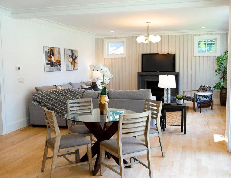 Bright living room and dining area with gray sectional, TV, and wood table under pendant light.