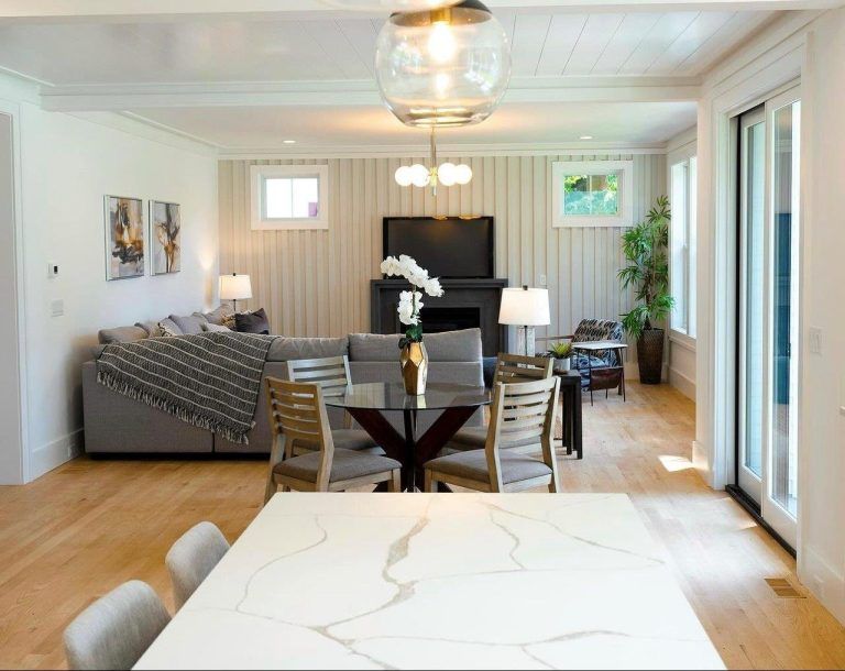 Bright modern living-dining room with gray sofa, black fireplace, wood floors, and sliding glass doors