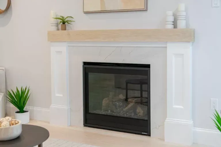 Modern living room fireplace with white mantel, light wood shelf, and small potted plants