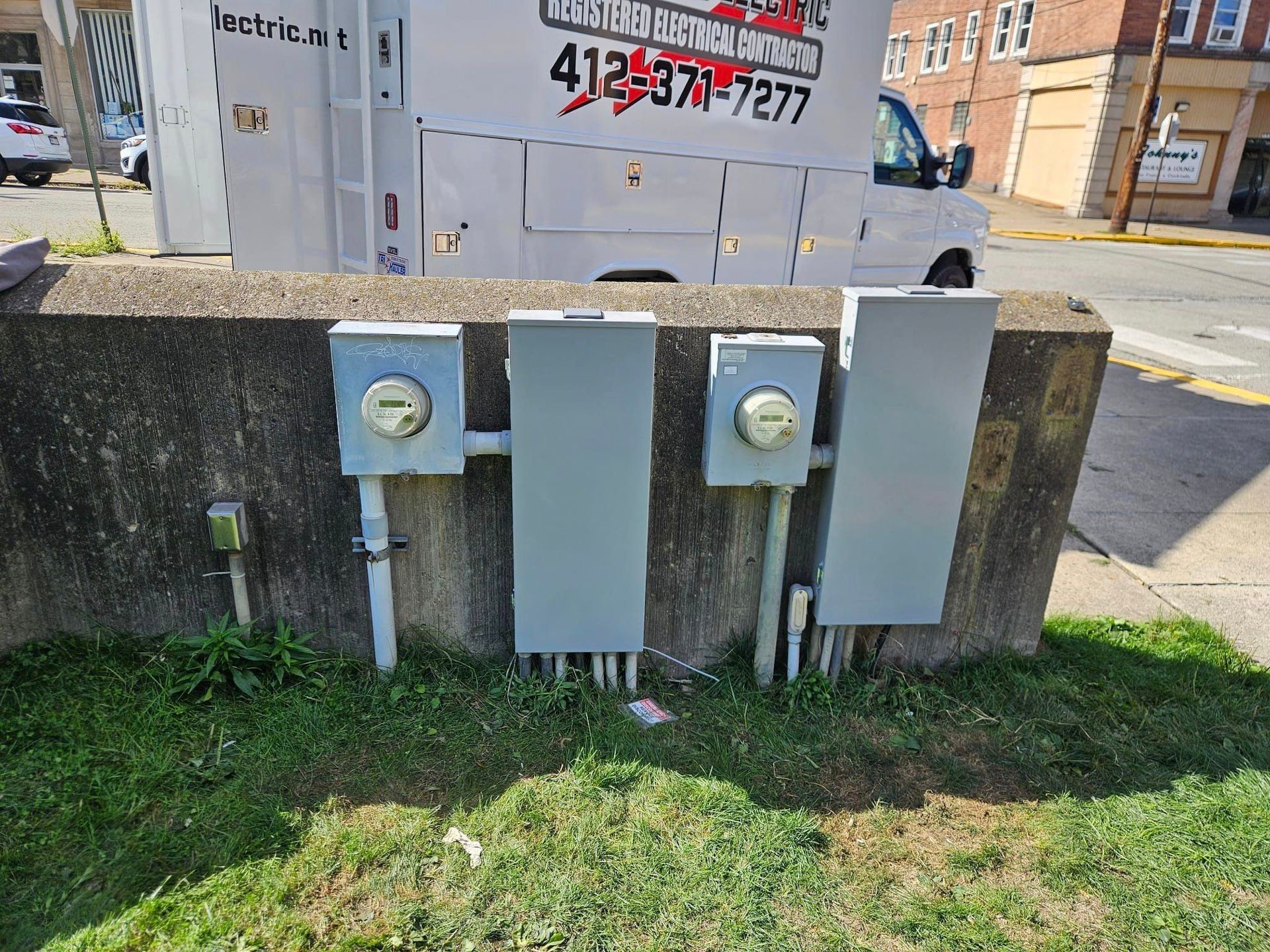 A white truck is parked next to a concrete wall with electrical panels attached to it