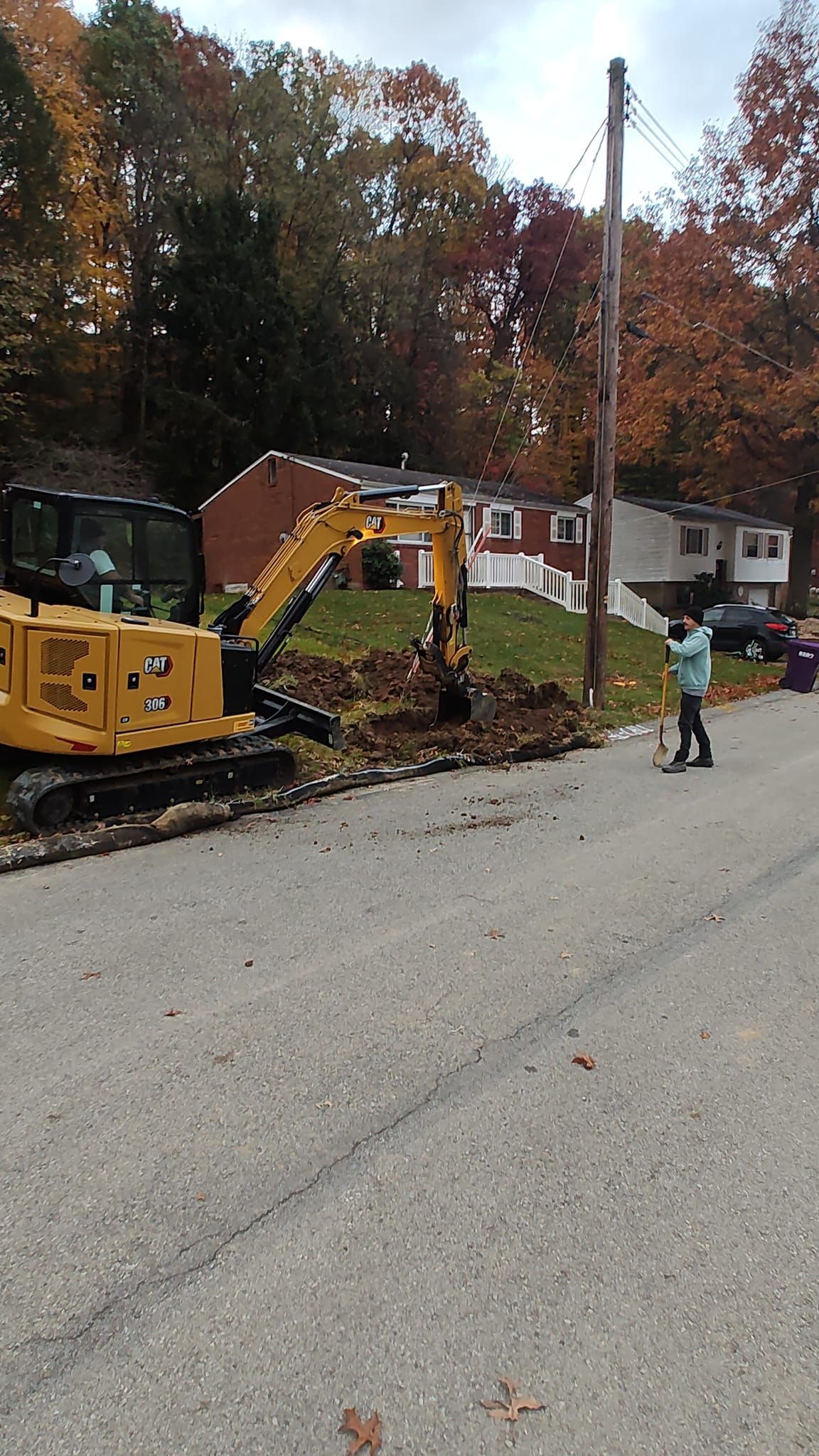 A little girl is standing on the side of the road next to a yellow excavator