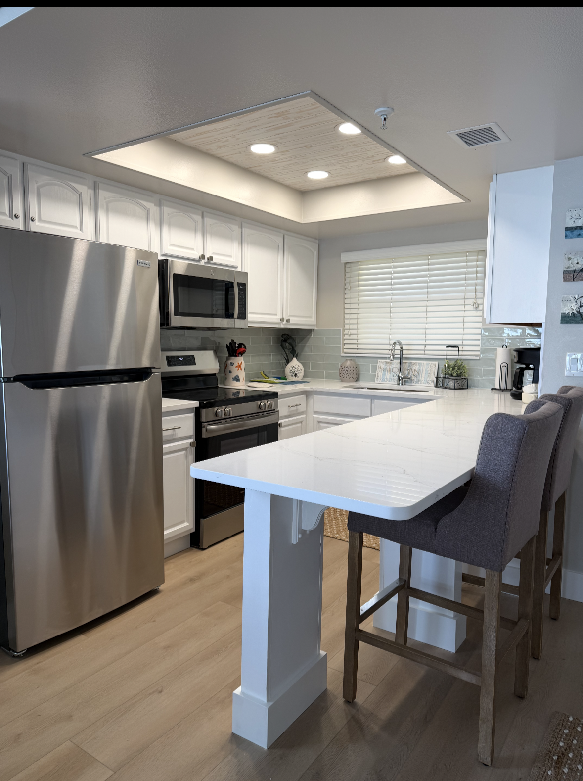 Modern kitchen with stainless steel appliances, white cabinets, and a breakfast bar with two gray stools.