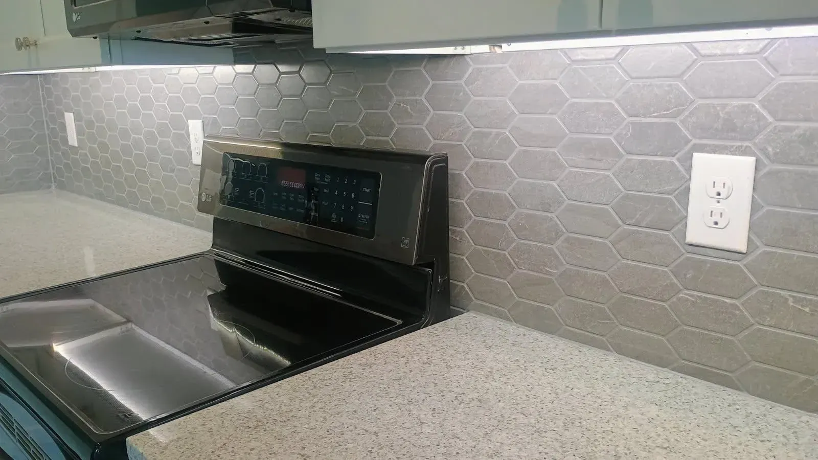 Kitchen with a stove, light gray countertops, and hexagon tile backsplash.