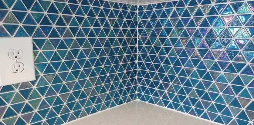 Blue triangular tiles on a wall with white grout. There's a white electrical outlet.