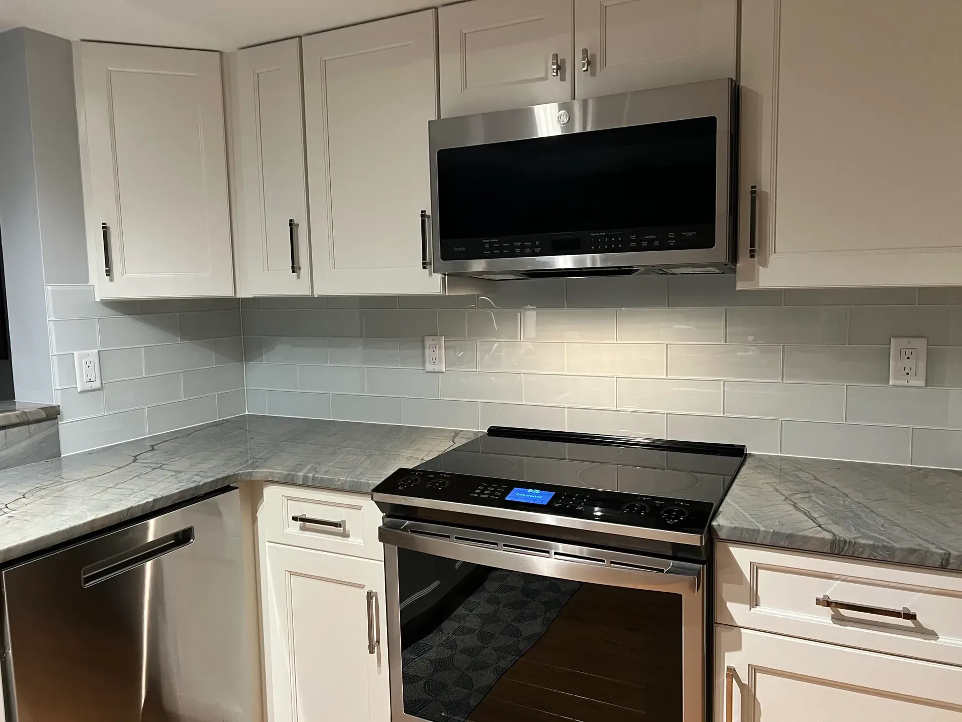 Kitchen with white cabinets, blue backsplash, stainless steel appliances, and gray countertop.