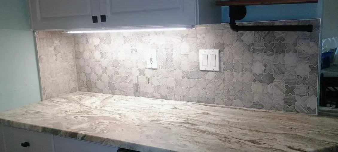 Kitchen countertop with granite surface, stone backsplash, and under-cabinet lighting.