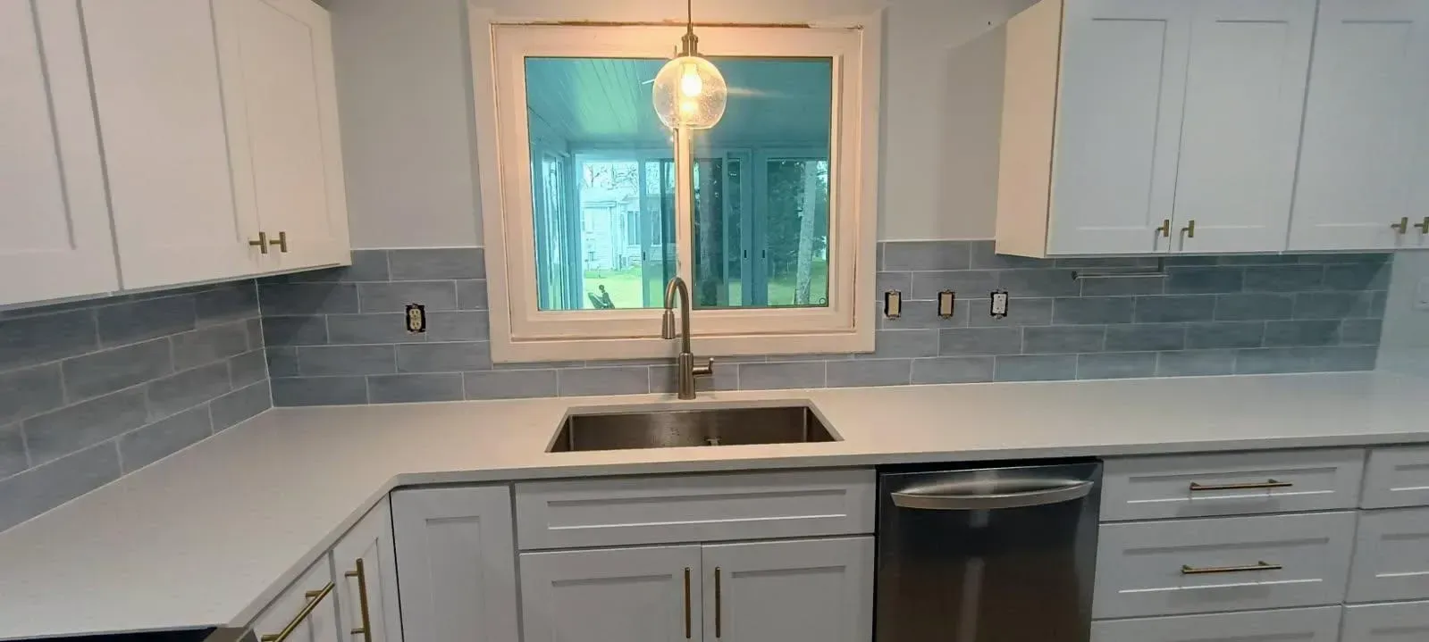 A newly renovated kitchen with white cabinets, gray backsplash, and a window above the sink.