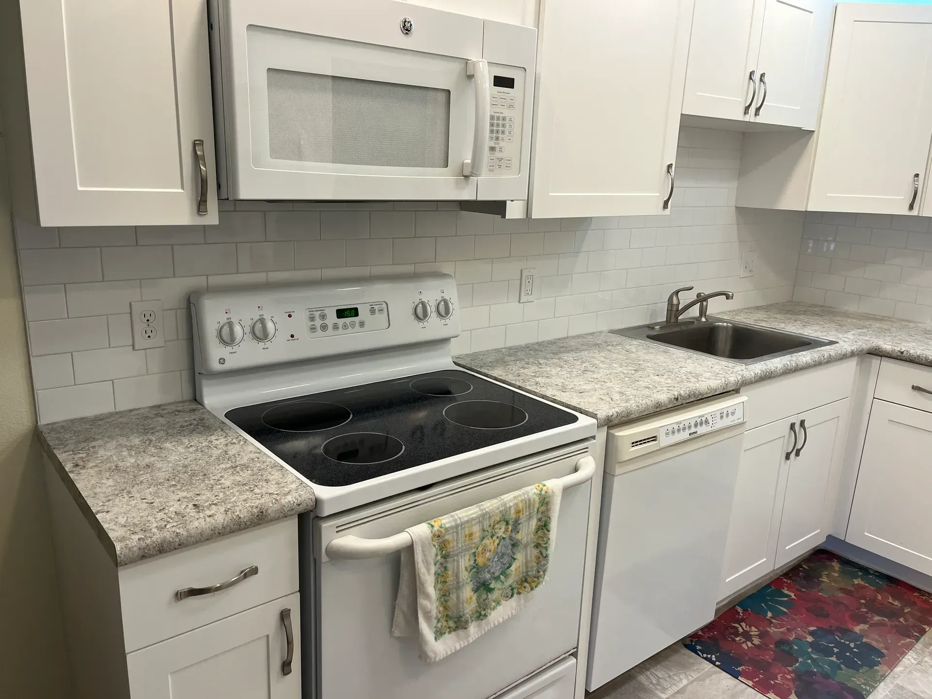 White kitchen with cabinets, stove, microwave, and sink; countertops have a speckled pattern.