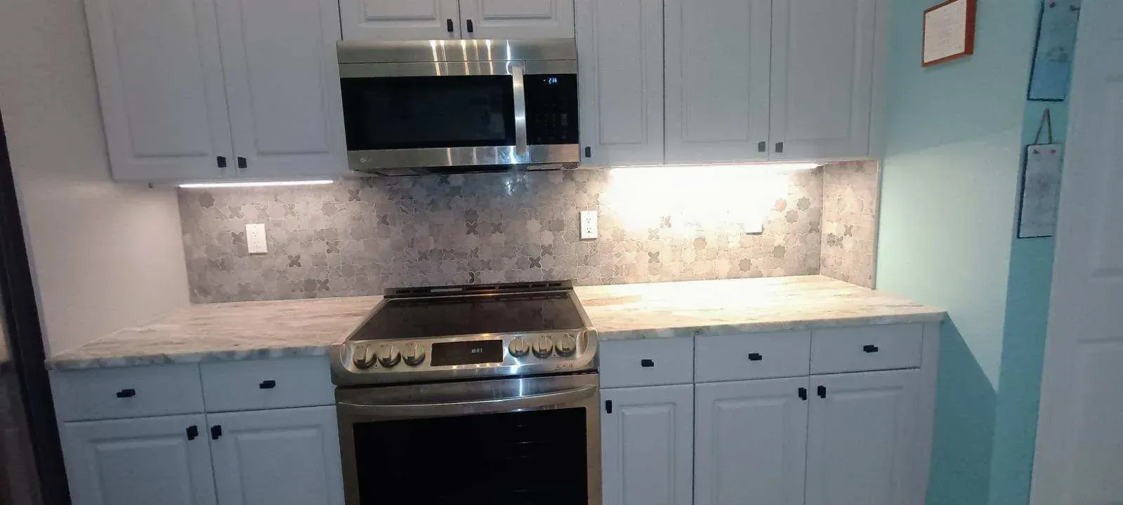 White kitchen cabinets with black hardware and a stainless steel oven and microwave.