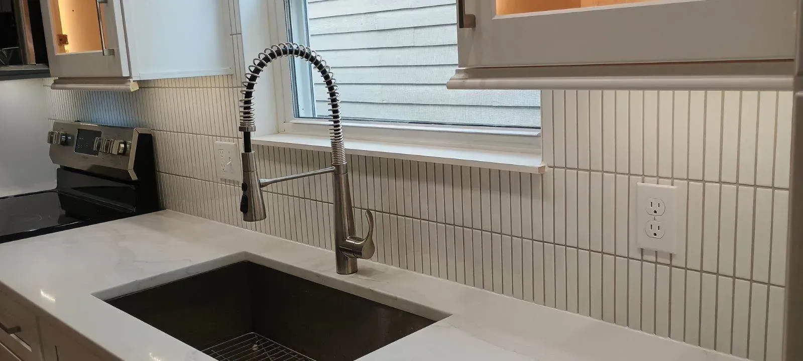 Kitchen sink with stainless steel faucet, white counter, and backsplash, with a window.