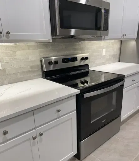 Kitchen with white cabinets, stainless steel appliances, and a light gray backsplash.