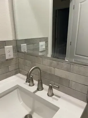 Bathroom sink with a brushed nickel faucet and soap dispenser, gray tile backsplash, and a large mirror.