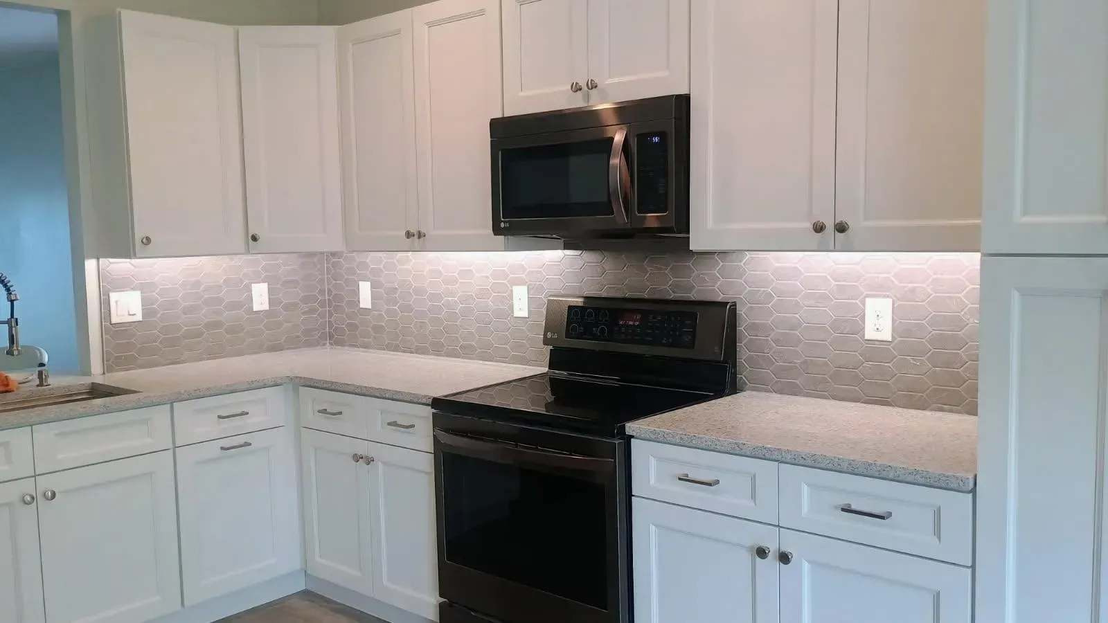 White kitchen cabinets with black appliances and mosaic backsplash.