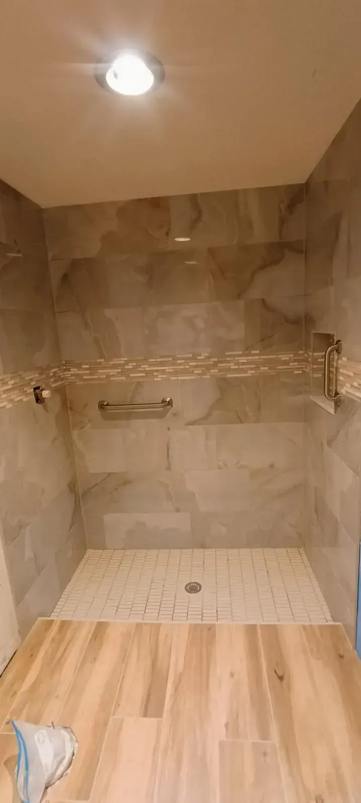 A newly tiled shower with light wood-look floor, stone-look walls, and a recessed ceiling light.
