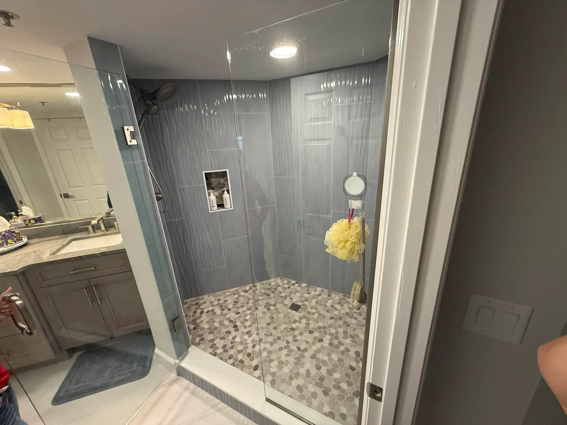 Shower stall with blue tiled walls, pebble floor, and glass door.