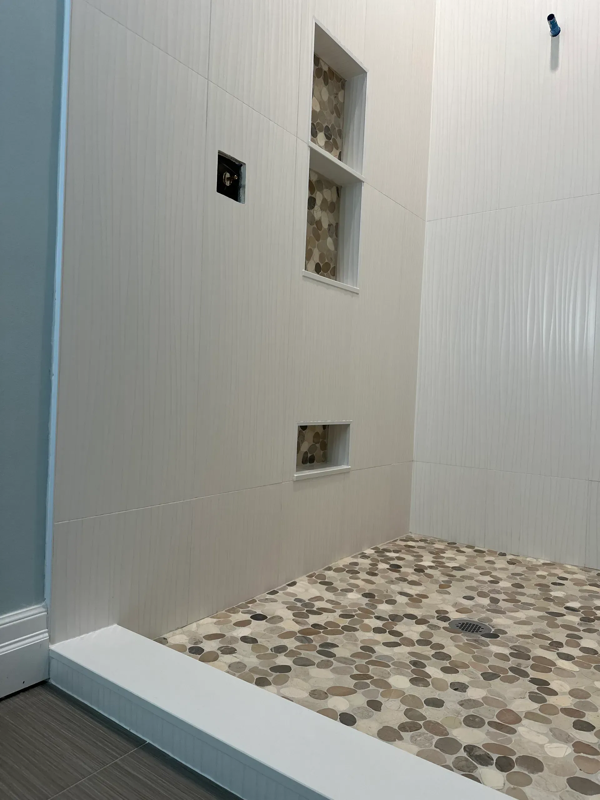 Shower with pebbled floor and white walls. Recessed shelves.